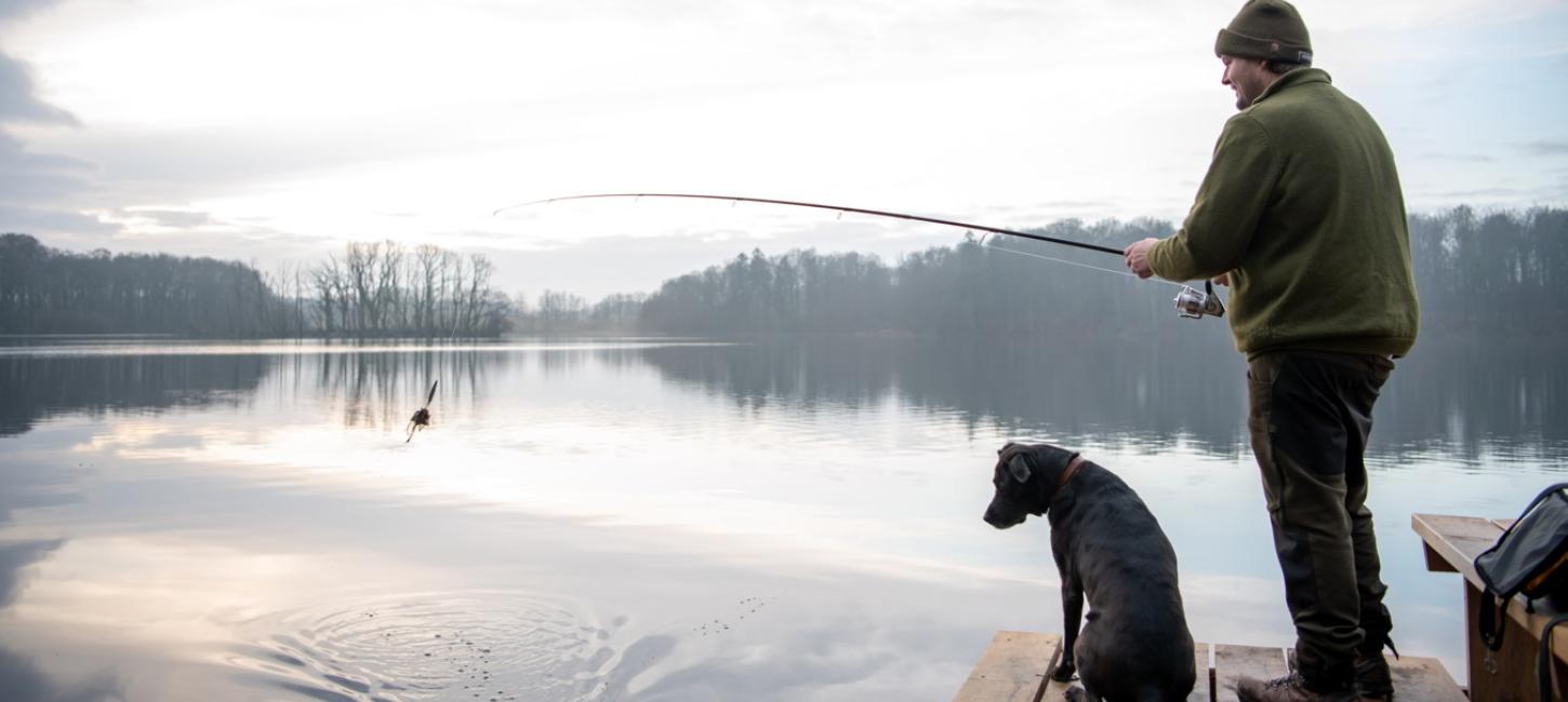 Mand og hund fisker ved en sø og kigger efter tang på en fiskekrog