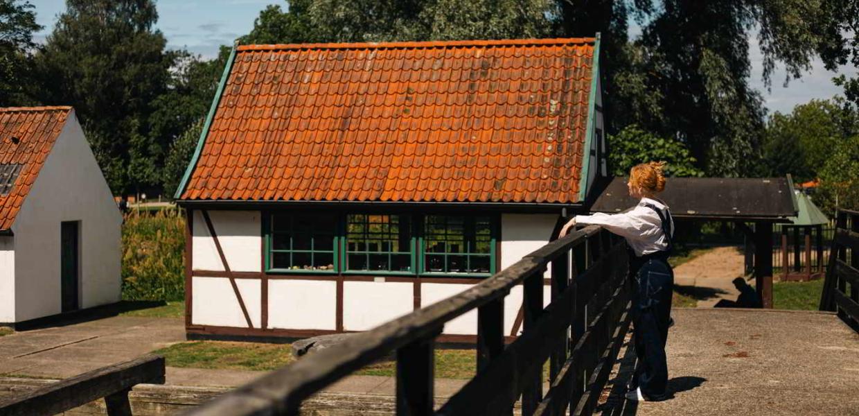 A young woman stands on a bridge and looks at a small half-timbered house in the Gunpowder Works Museum.