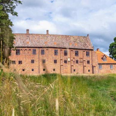 Esrum Monastery's red brick building is located at the end of a large grassy field.